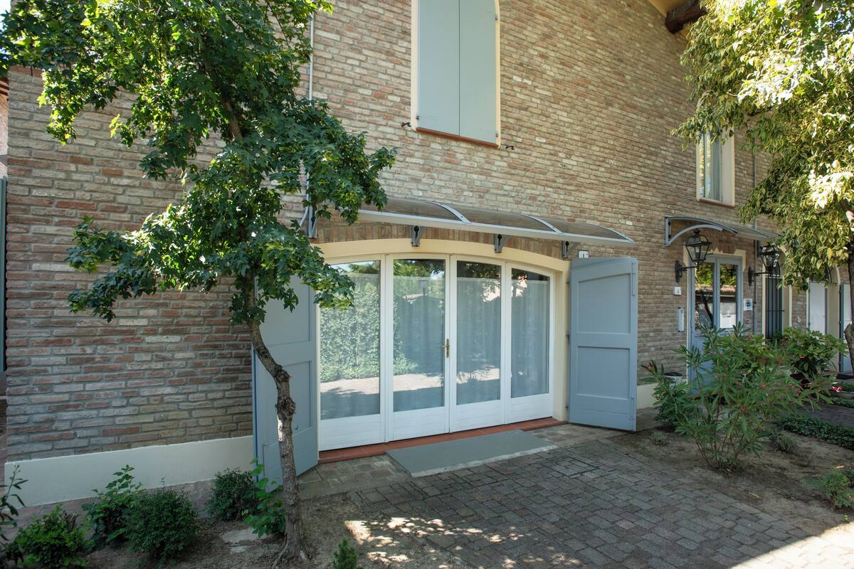 A brick building with a large glass door entrance, a covered porch, and a small garden area.