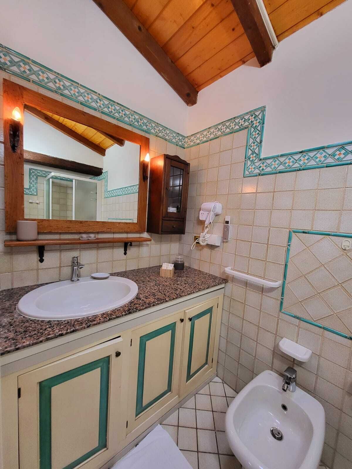 A bathroom with two sinks, a mirror, a cabinet, a bidet, and a towel rack.