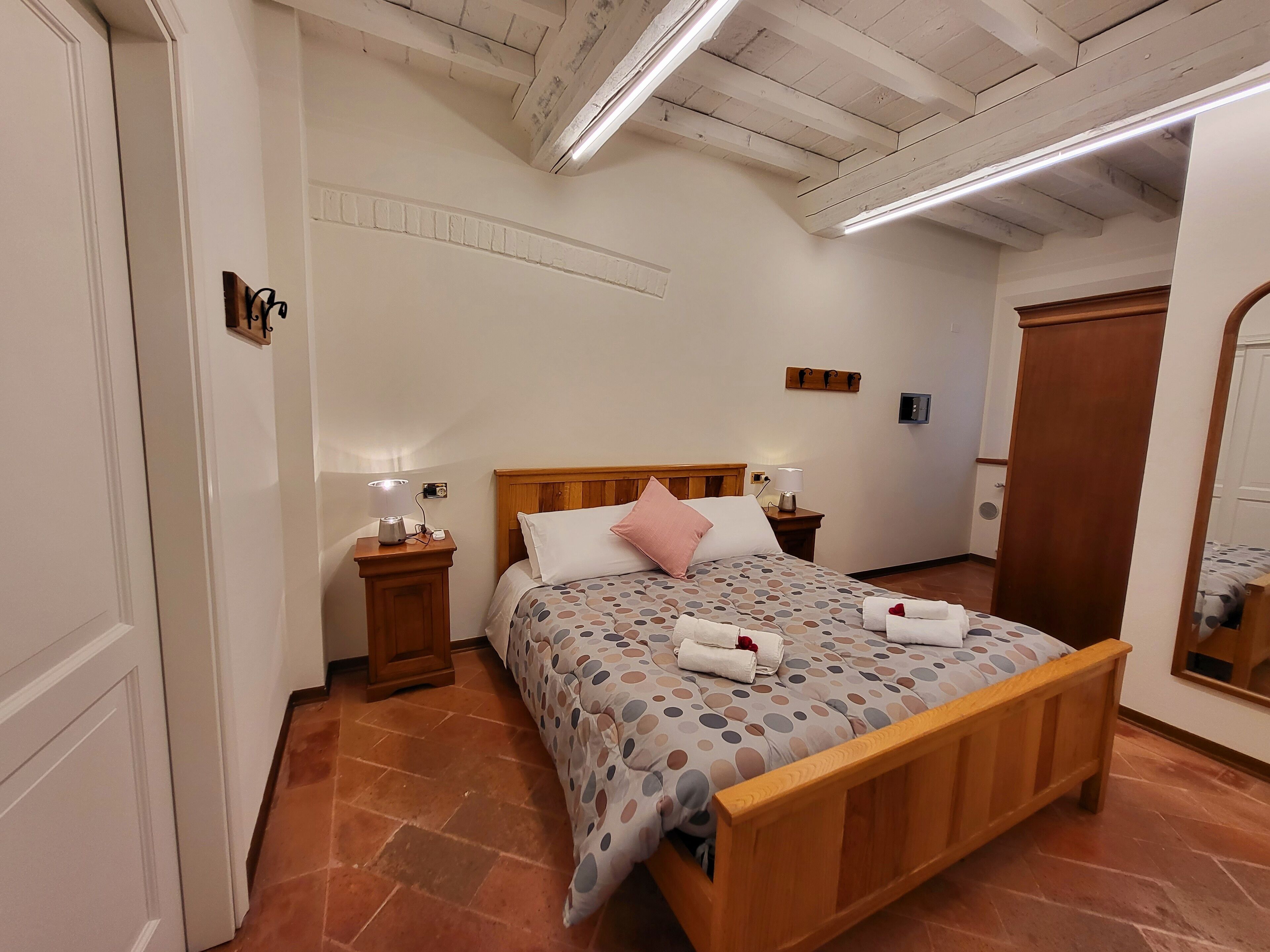 A bedroom with a wooden bed, two bedside tables with lamps, a mirror, and a wardrobe.