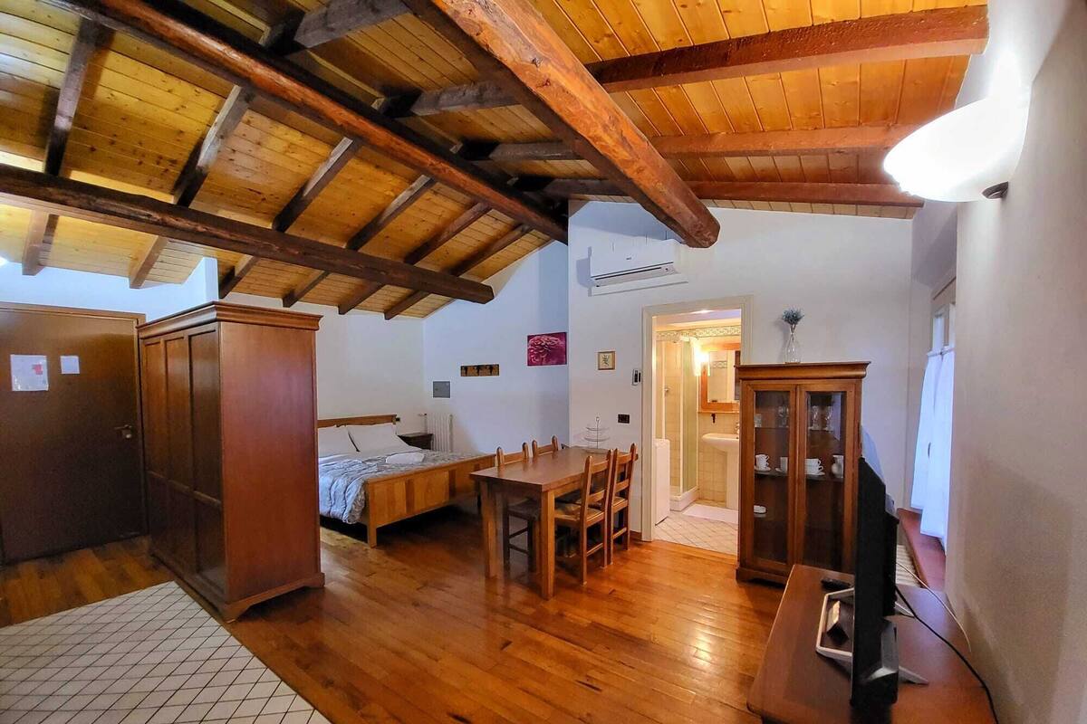 A room with a wooden ceiling, a bed, a dining table with chairs, a cabinet, and a television.