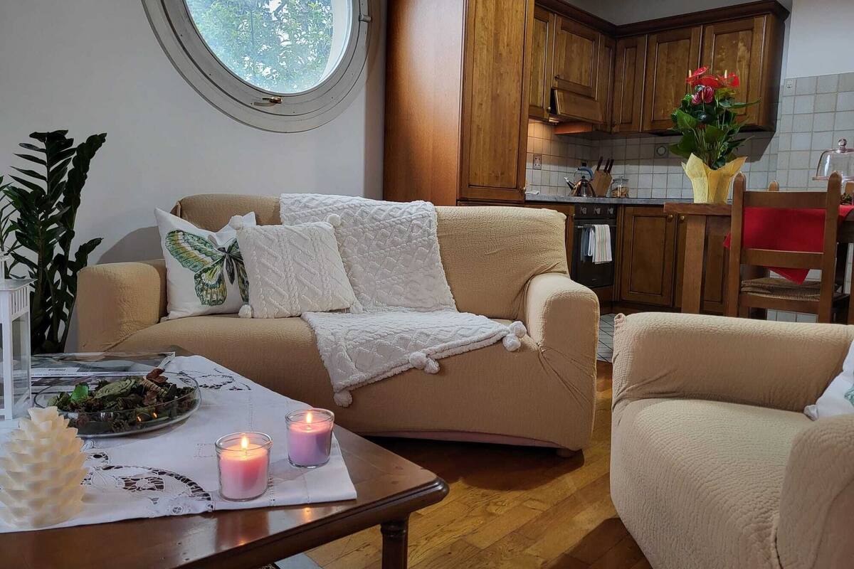 A cozy living room with a beige sofa, a round window, wooden cabinets, and a dining table with candles.