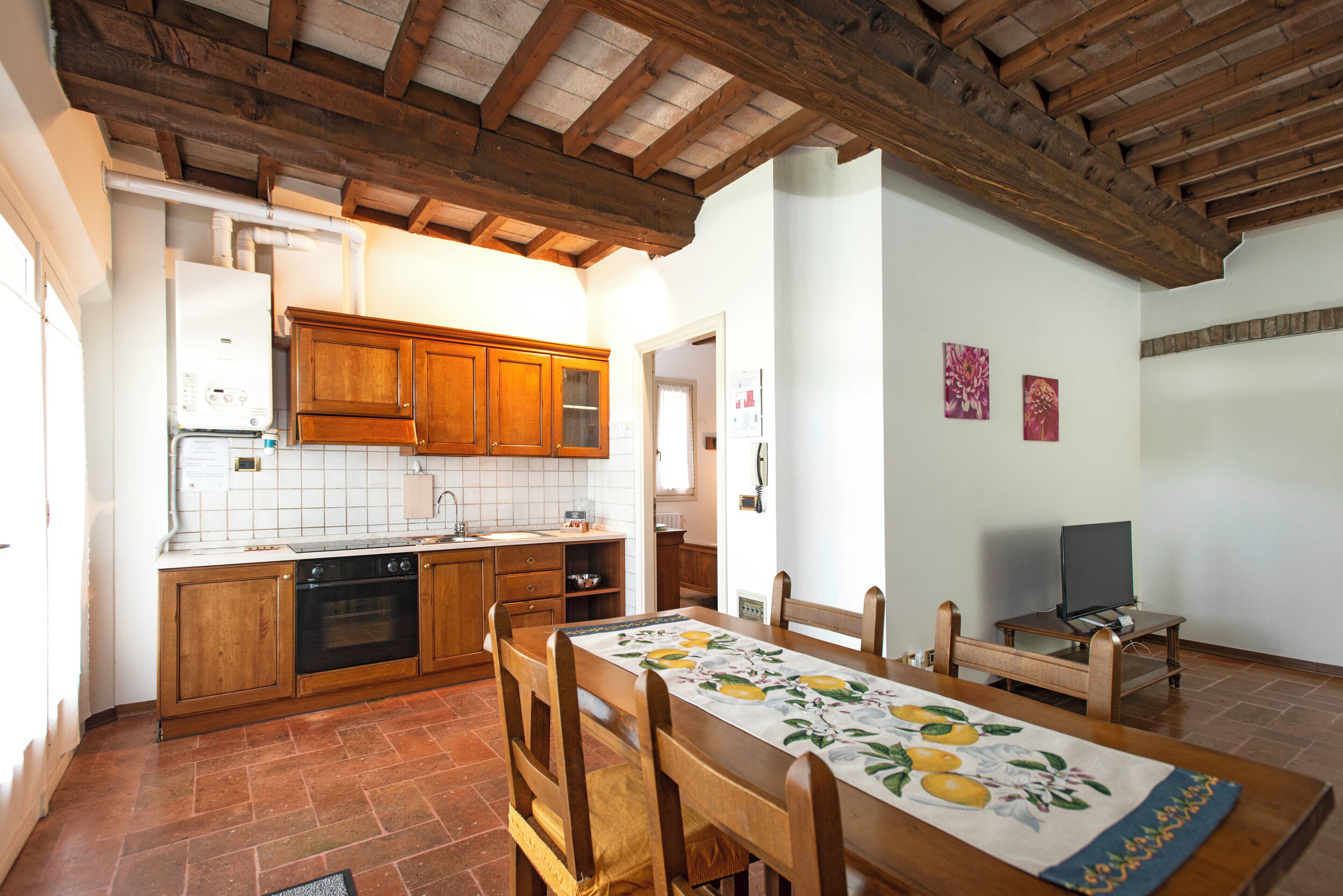 A kitchen with wooden cabinets, a built-in oven, and a dining area with a table set for four.