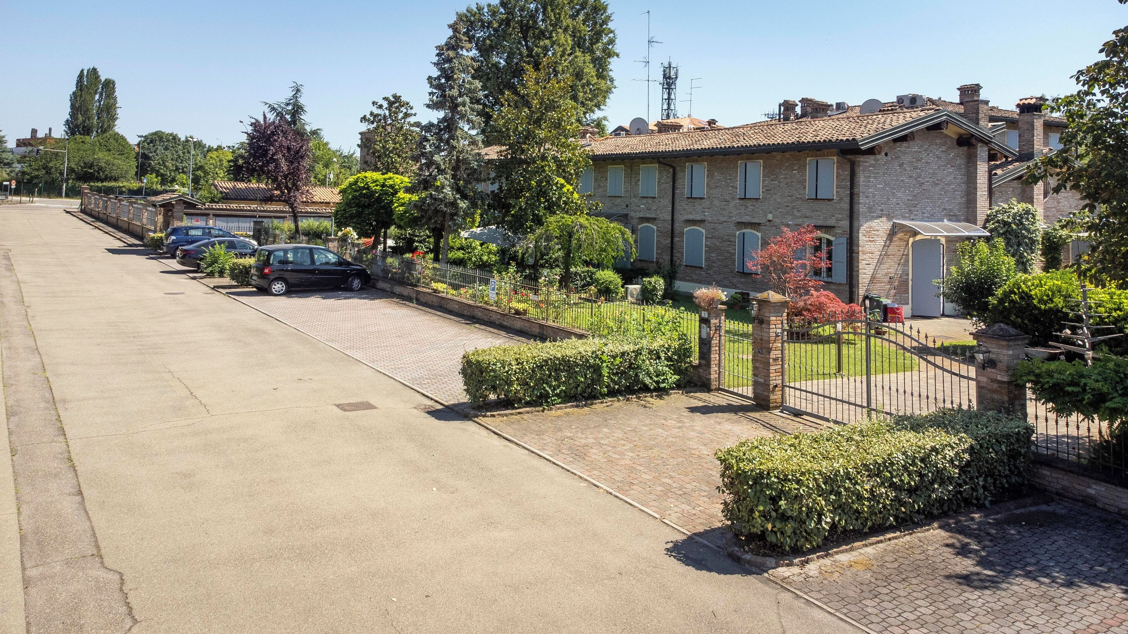 Una strada residenziale con case, auto parcheggiate e cielo sereno.