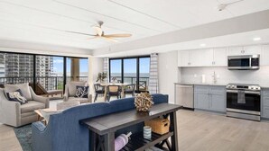Un appartamento moderno con soggiorno, zona pranzo e cucina. Dispone di ampie finestre, un balcone e una ventola a soffitto.