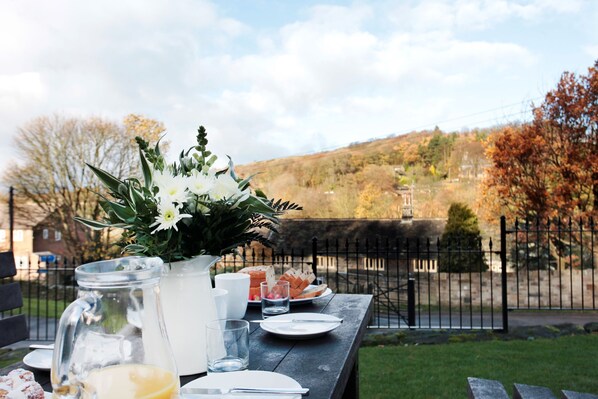 A picnic table set outdoors with a view of a hill and a fence.