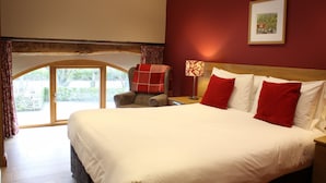A hotel room with a large bed, a chair with a red blanket, a nightstand with a lamp, and a framed picture on the wall. - Unsliven Bridge Farm - sleeps 15 guests  in 7 bedrooms (Stocksbridge)
