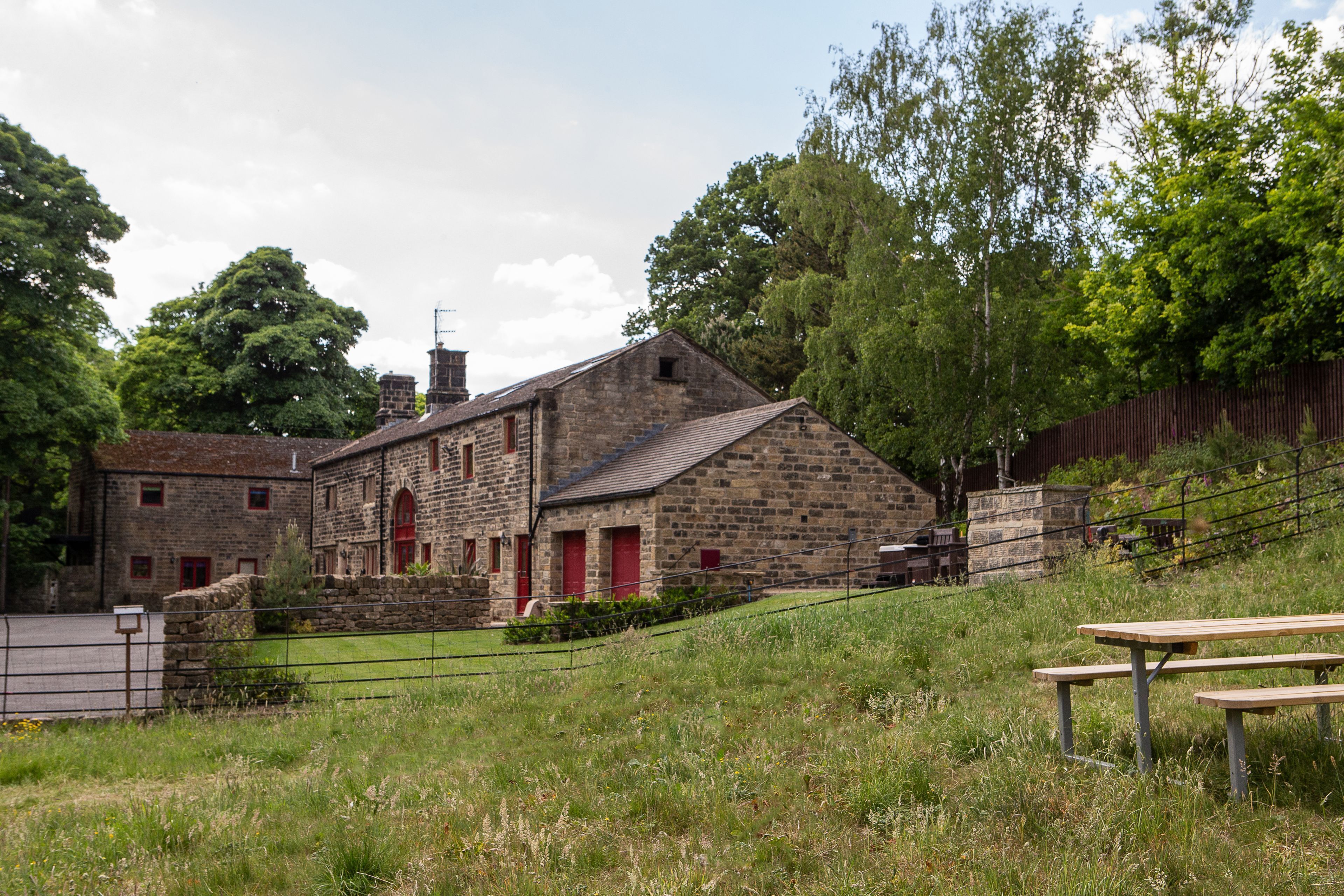 A stone building with red doors and windows, a picnic table, and a grassy area.