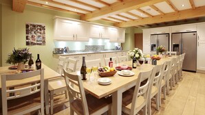 A spacious kitchen with wooden beams, white cabinets, and a dining area with white chairs and a long table set for a meal. - Unsliven Bridge Farm - sleeps 15 guests  in 7 bedrooms (Stocksbridge)