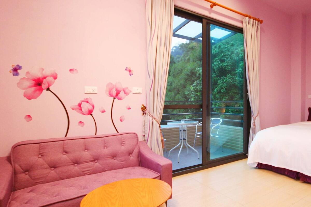 A pink-themed bedroom with a sofa, a bed, and a balcony with a glass door.