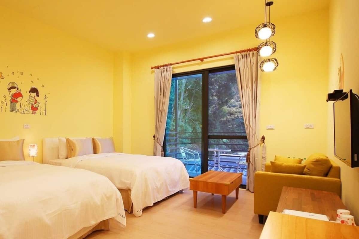 A hotel room with two beds, a sofa, a small table, and a window with curtains.
