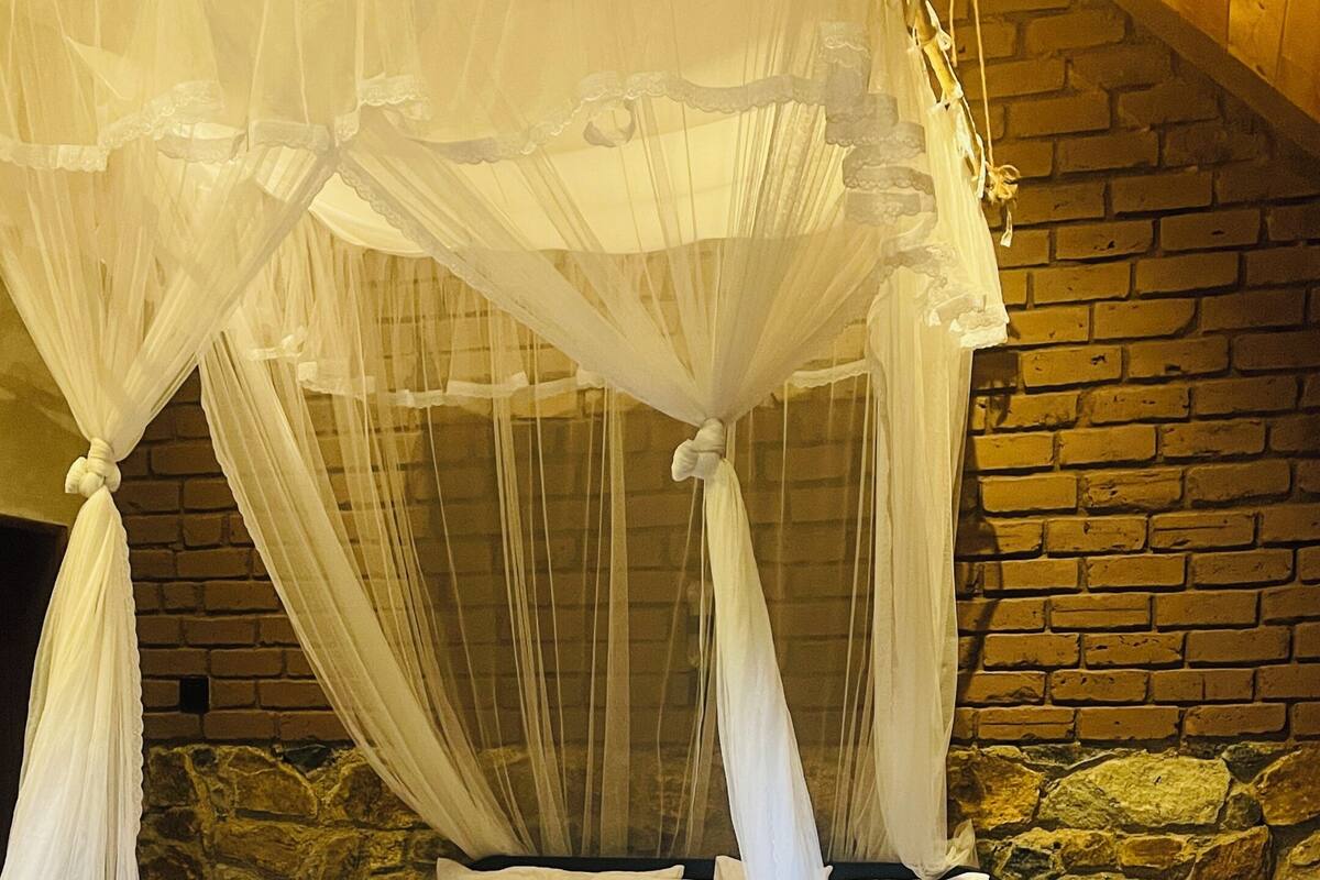A bed with a canopy, a stone wall, and a wooden floor.