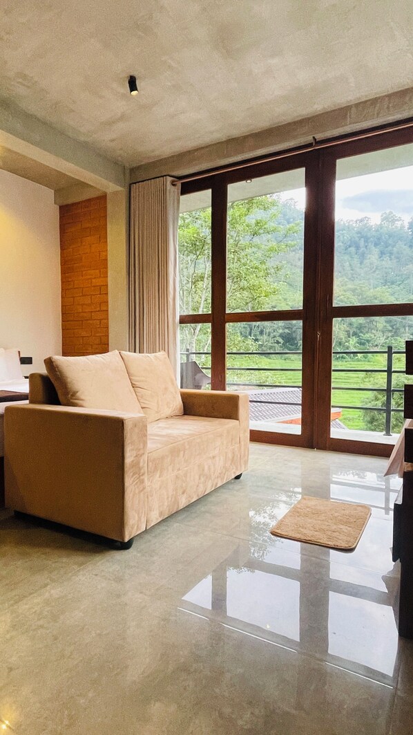 A modern living room with a beige sofa, a flat-screen TV, and a large window offering a view of a lush landscape. - Wild resort Ella  (Ella)