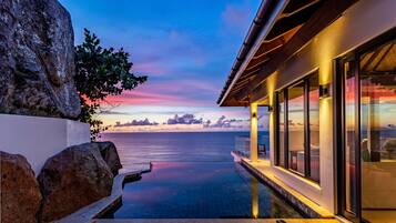 Relax by the serene pool overlooking a calm body of water, surrounded by comfortable seating and beautifully maintained gardens.