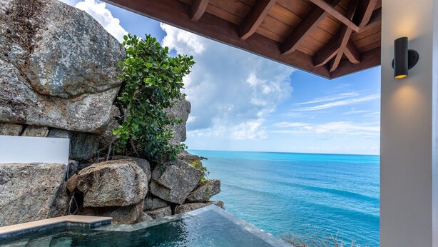 A pool with clear blue water, surrounded by large rocks and greenery, overlooking a turquoise sea under a wooden ceiling. - Maxi Cooper Bay (Road Town)
