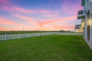 Un prato verde con una recinzione bianca a paletti, un edificio a più piani e un cielo al tramonto.