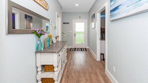 Un couloir doté d’un plancher en bois, une console blanche ornée d’un vase de fleurs, un miroir et une enseigne indiquant « Beach House ».