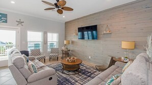 Un salon doté d’un ventilateur de plafond, d’un grand téléviseur à écran plat et d’un mur en bois. On y trouve deux fauteuils, un canapé et une table basse.