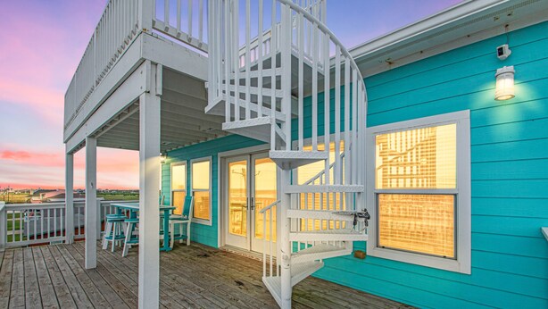 Un bâtiment turquoise doté d’une terrasse en bois, d’un escalier en colimaçon blanc et offrant une vue sur l’océan.