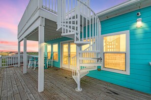 Ein türkisfarbenes Gebäude mit einer Holzdachterrasse, einer weißen Wendeltreppe und Blick aufs Meer.