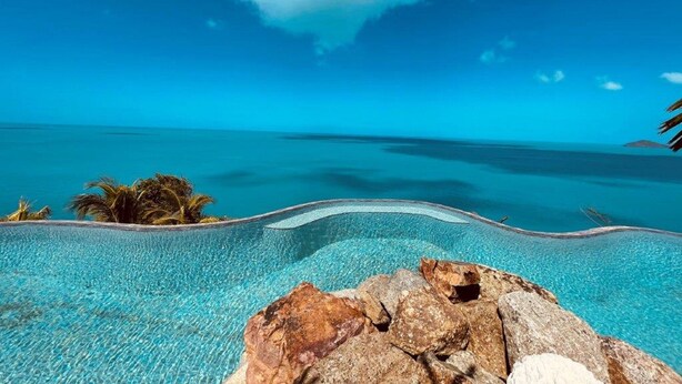 A clear blue sky, a pool with a rocky edge, and a view of the ocean. - MyALL Tortola (Road Town)
