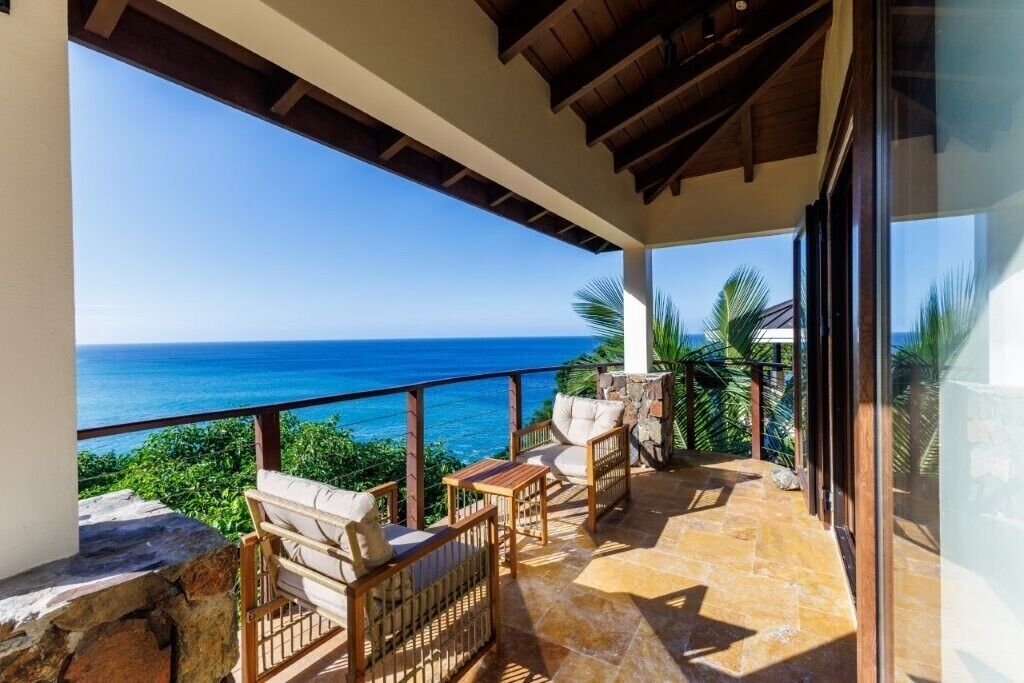 A balcony with a view of the ocean, stone flooring, and wicker furniture.