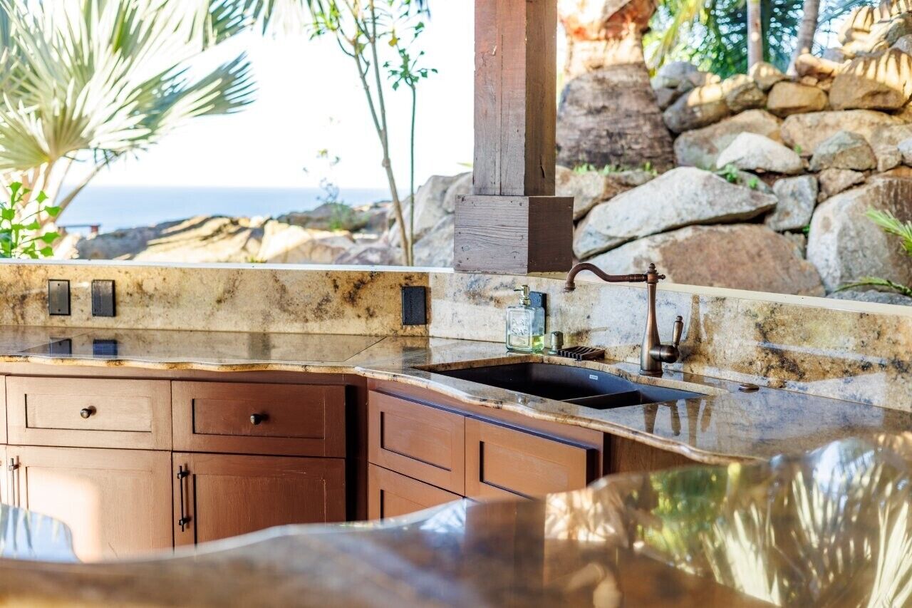 An outdoor kitchen with a stone countertop, wooden cabinets, and a view of the ocean.