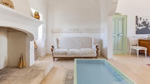 Una habitación con un sofá blanco, una puerta verde, una chimenea y una piscina.