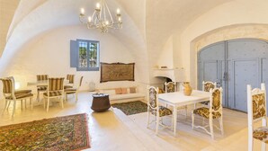 Una habitación amplia con un techo alto abovedado, una araña, una mesa de comedor con sillas, un sofá y una puerta azul grande.