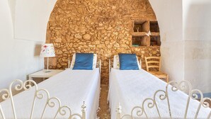 Una habitación con dos camas, una pared de piedra y una mesita con una lámpara.
