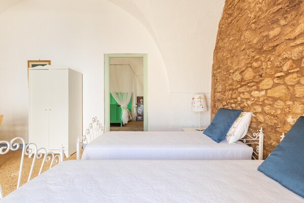 Un dormitorio con dos camas, un armario, una pared de piedra y un acceso a otra habitación.