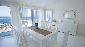 A bright, white room with a balcony overlooking the sea. There is a dining table with chairs and a white cabinet with drawers. - Attico Barca by BarbarHouse (Gallipoli)