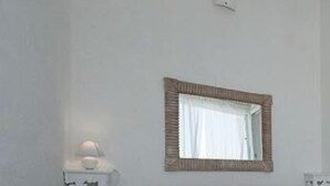 A minimalist bedroom with a single bed, a bedside table with a lamp, and a mirror on the wall. - Attico Barca by BarbarHouse (Gallipoli)