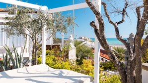 A terrace with white railings, olive trees, and a view of the sea.