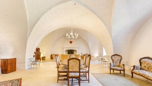A spacious interior with a high arched ceiling, a chandelier, a dining area with chairs and a table, and a sofa.
