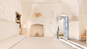 A spacious bedroom with a large bed, a wooden chair, and a small table with a lamp.