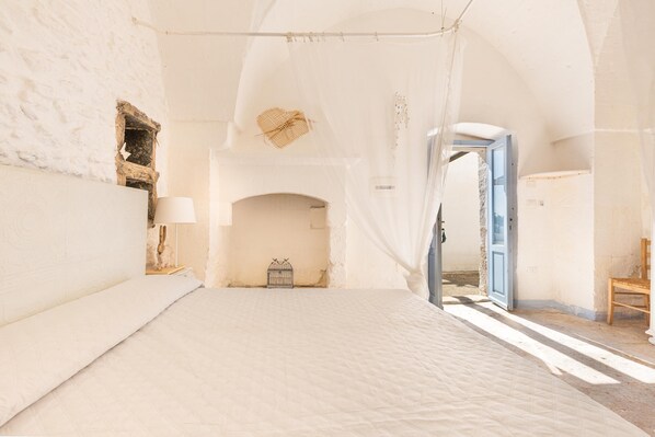 A spacious bedroom with a large bed, a wooden chair, and a small table with a lamp.