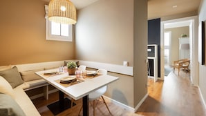 A modern dining area with a white table set for two, a woven pendant light, and a view into the kitchen. - Ola Living Diagonal B 4-2 (Barcelona)