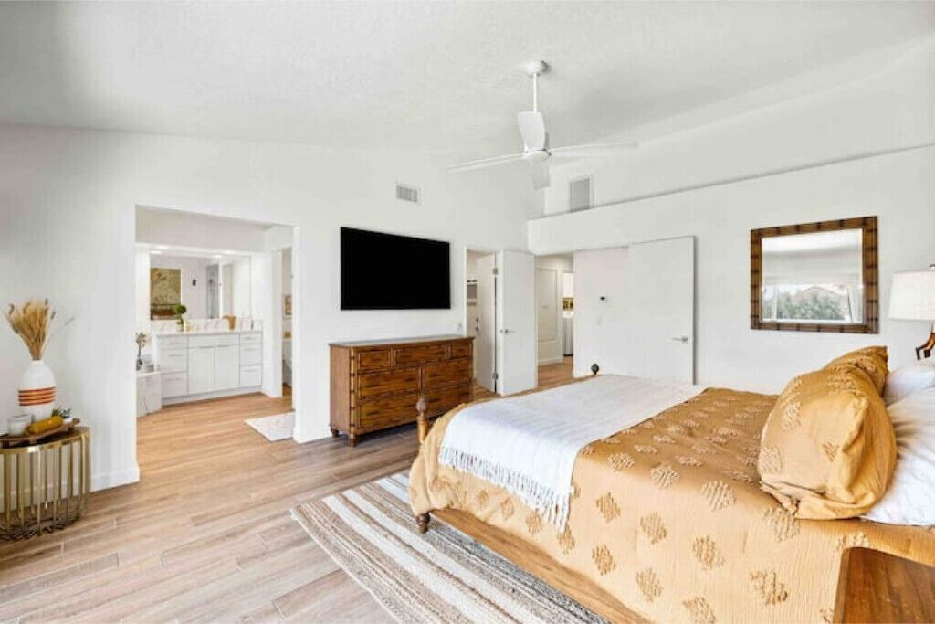 Een slaapkamer met een bed, een dressoir, een televisie en een spiegel.