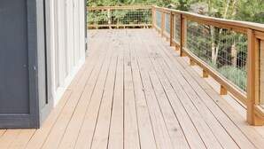 A wooden deck with a railing, a white ceiling, and a view of trees in the background.
