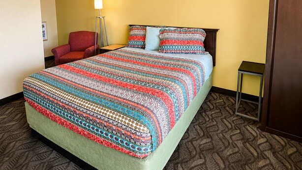 A hotel room with a bed, a chair, a bedside table, and a lamp. - Vernals Best Value Inn (Vernal)