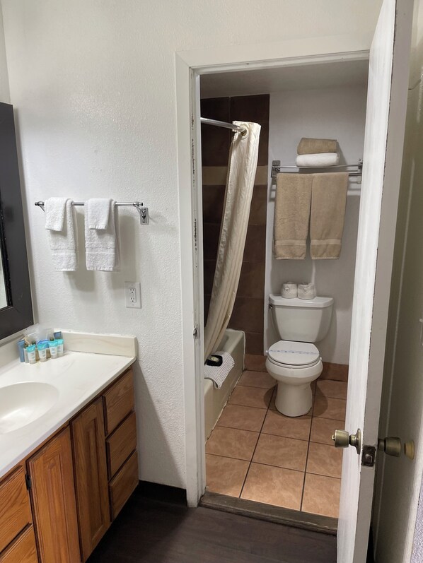 A bathroom with a white sink, wooden cabinets, a shower curtain, and a toilet. - Vernals Best Value Inn (Vernal)