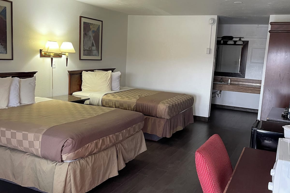 A hotel room with two beds, a desk, a chair, a lamp, and a mirror.