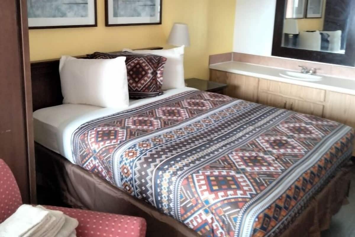 A hotel room with a bed, a desk, a chair, a mirror, and artwork on the wall.
