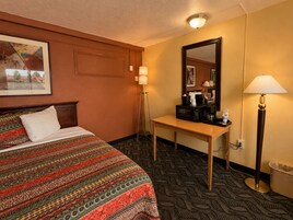 Una habitación de hotel con cama, escritorio, espejo y cubo de basura.