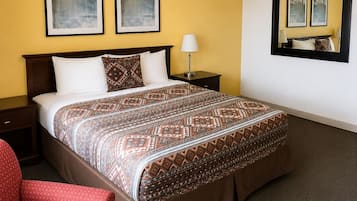Une chambre d’hôtel avec un lit, une table de chevet, une chaise, une lampe et deux tableaux encadrés au mur.