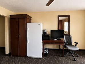 A hotel room with a wooden wardrobe, a white refrigerator, a desk with a computer and a chair, and a mirror on the wall. - Vernals Best Value Inn (Vernal)