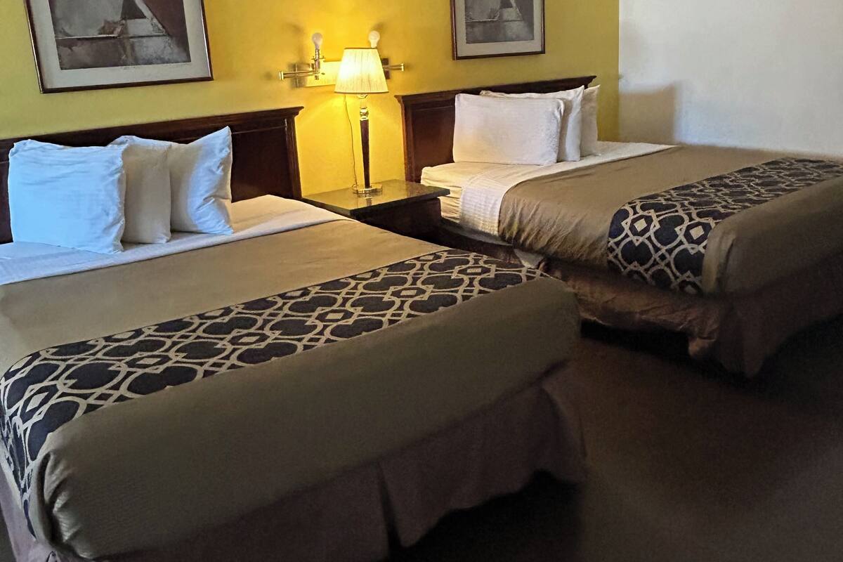 A hotel room with two beds, a ceiling fan, and two framed pictures on the wall.