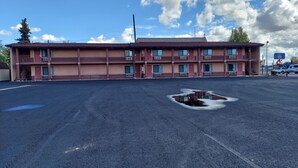 Un motel de dos pisos con fachada roja, varios balcones y un estacionamiento con un charco.