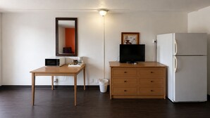 A small kitchenette with a microwave, a refrigerator, a wooden table, a cabinet with drawers, a trash bin, and a wall-mounted mirror. - Vernals Best Value Inn (Vernal)