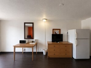 A small kitchenette with a microwave, a refrigerator, a wooden table, a cabinet with drawers, a trash bin, and a wall-mounted mirror. - Vernals Best Value Inn (Vernal)